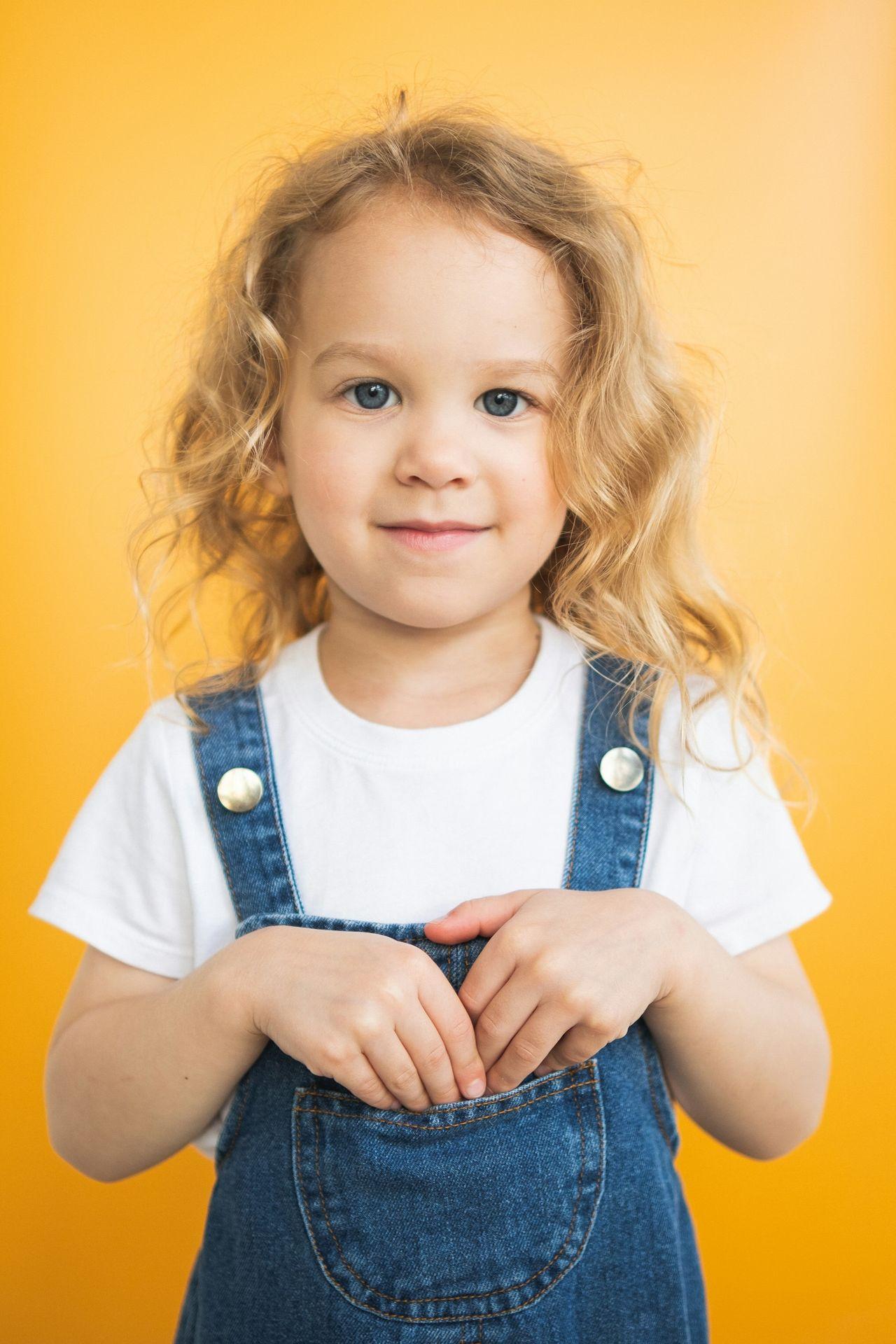 a little girl in overalls posing for a picture